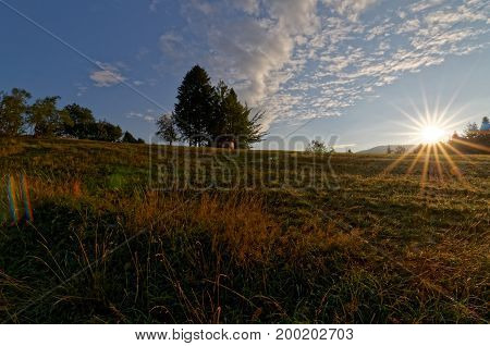 Sunrise over country meadow. Beautful clouds on the blue sky. Trees in the background. Poland.