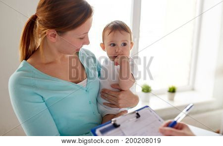 medicine, healthcare, pediatry and people concept - happy woman with baby and doctor with clipboard at clinic