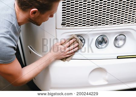 A close-up of a car washer wipes the lights with a sponge truck or bus replacement of candles, concept repair in a garage, car repair shop