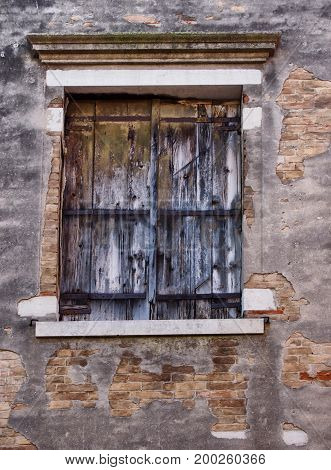 old wooden shuttered window with faded peeling black paint in an ancient brick wall with peeling broken grey cement or plaster