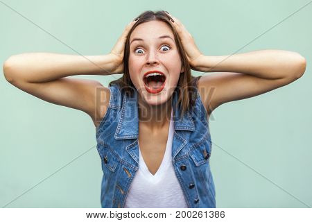 Wow! Can not be! Positive emotions and feelings. The beautiful girl shocked and wounder touching her head her hands and looking at camera. Indoor studio shot