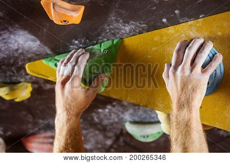 Closeup of rock climber's hands gripping handholds in indoor climbing gym