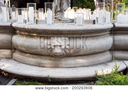Fountain decorated with lion head statue and candles. Wedding ceremony decoration details. Fountain with statues in outdoor restaurant