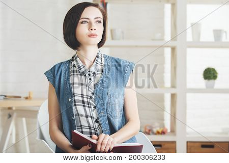 Portrait of pretty young woman reading book in modern office interior. Knoweldge information education and leisure concept