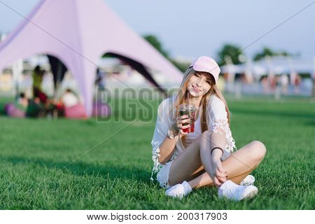Portrait of a smiling girl resting on a green lawn and drinking cold lemonade. Summer concept. Rest in the park