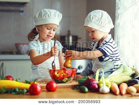 Healthy eating. Happy children prepares and eats vegetable salad in kitchen