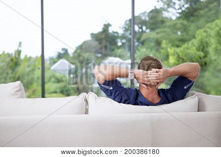 portrait of youg man with hands behind his head is relaxing on couch
