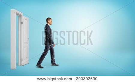 A businessman on blue background walking through an open white doorframe. New business ventures. Entering new market. Career growth.