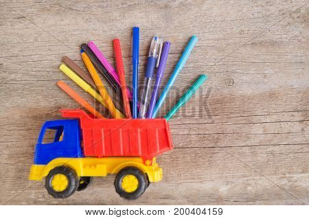 Colorful felt-tip pens and ball pens in the toy truck on the wooden table. Space for text