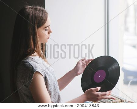 Girl choosing retro vinyl records in music shop. Modern hipster style, young female melomaniac