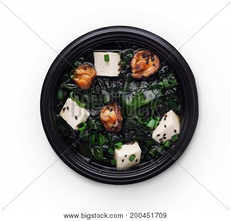 Japanese food delivery. Miso soup with tofu cheese, mushrooms and seaweed in black take away plate isolated at white background, top view