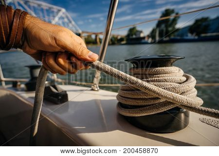 The man's hand holds the end of the rope wound on the small windlass of the yacht ship.