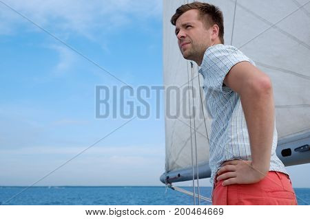 Young caucasian sailor relaxing happily on sailboat yacht. He loooks aside and dream. Active summer vacation.