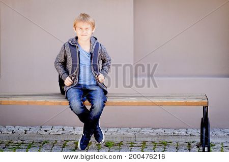 Child with backpack sitting on the bench near the school