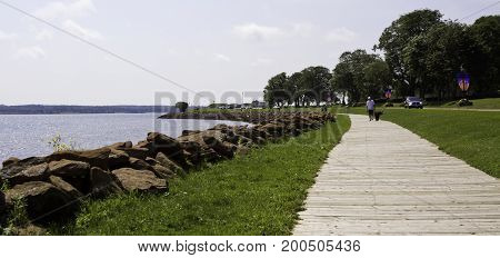 Charlottetown, Prince Edward Island - August 21, 2011 - Wide view of a man walking his dog on a long wooden path along the Northumberland Straight shoreline in Charlottetown, Prince Edward Island on a bright sunny day in August.