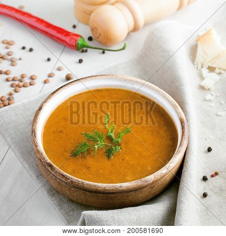 Lentil soup in a rustic bowl and a piece of bread on a cotton canvas tablecloth. Healthy vegetarian food on a white wooden table.