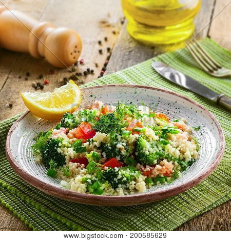 Plate with couscous and vegetables on a rustic wooden table. Traditional eastern healthy meal made of couscous broccoli tomato pepper onion and dill.