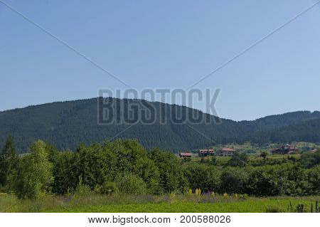 Scene with mountain top, forest, glade and residential district of bulgarian village Beli Iskar, Rila mountain, Bulgaria