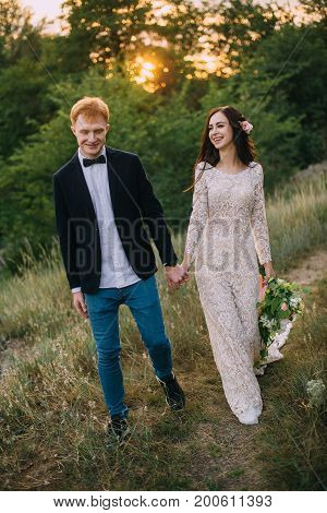 Happy newlyweds holding hands and walking in nature