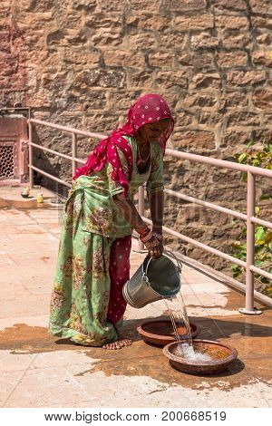 JODHPUR RAJASTHAN INDIA -MARCH 05 2016: Vertical picture of Indian woman spilling water at Mehrangarh Fort in Jodhpur the blue city of Rajasthan in India.
