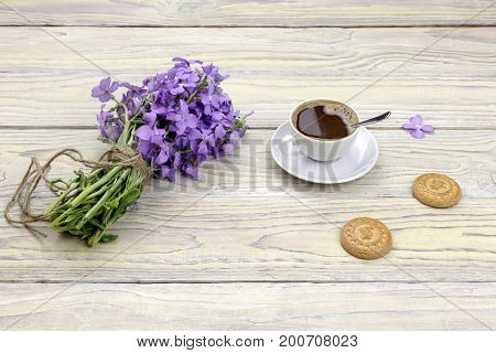 A cup of coffee and a bouquet of gillyflower on a wooden table close-up