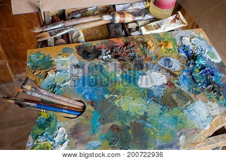 The artist's palette covered with colors with tassels lying on the sketchbook.