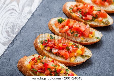Appetizer bruschetta with chopped vegetables on ciabatta bread on stone slate background close up. Delicious snacks sandwiches crostini canape antipasti on party or picnic time. Top view