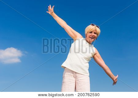 Low-angle view of a fit senior woman looking up to the sky with outstreched arms while enjoying retirement in a sunny day of summer