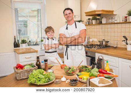 Chef man cooking salad on the kitchen with little son. Paranting concept.