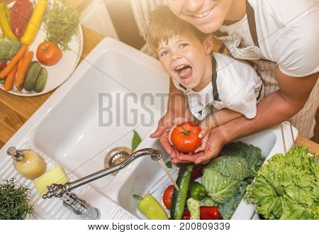 Father with little son washes vegetables on the kitchen before eating