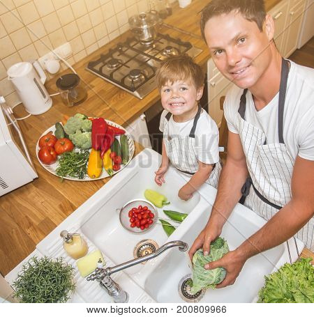 Father with little son washes vegetables on the kitchen before eating