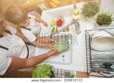 Father with little son washes vegetables on the kitchen before eating