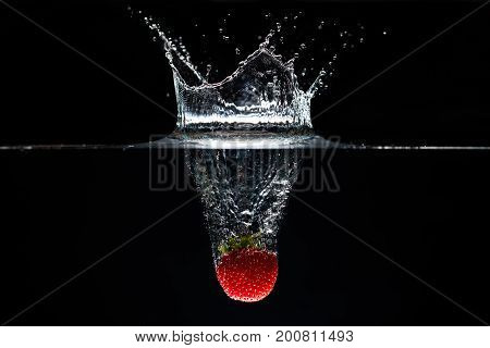 A strawberry splashing into water black background.