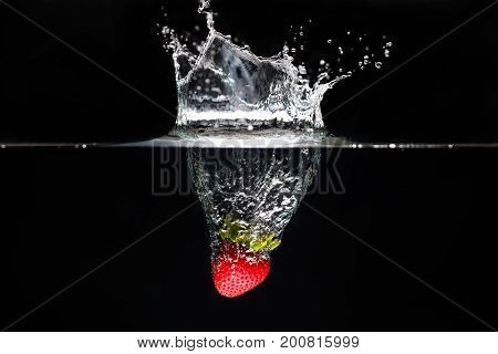 A strawberry splashing into water black background.