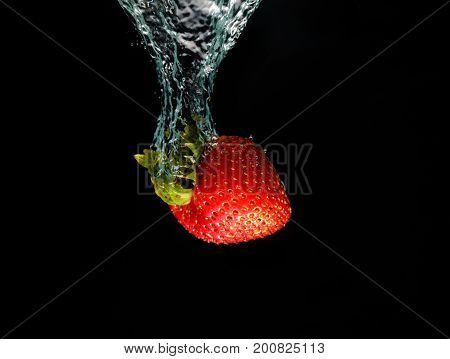 A strawberry splashing into water black background.