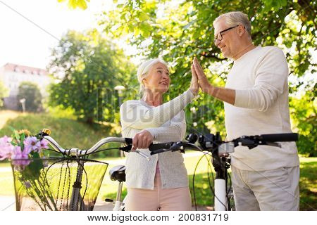 old age, people and lifestyle concept - happy senior couple with fixie bicycles making high five at summer city park