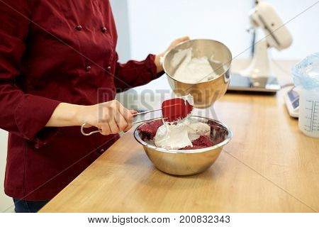 cooking, baking, food and people concept - chef adding whipped egg whites to macaron batter in bowl at pastry shop kitchen