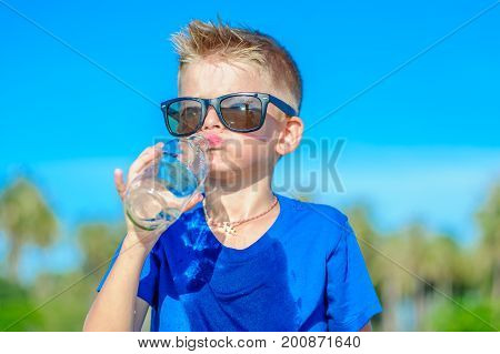 Portrait Of A Thirsty Handsome Boy In Sunglasses Drinking Water On The Desert Tropical Beach