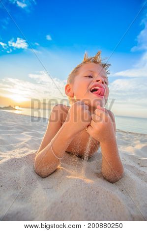 Handsome Eight Years Boy On Beach Performs Acrobatic Sketches And Plays With A Stream Of Sand