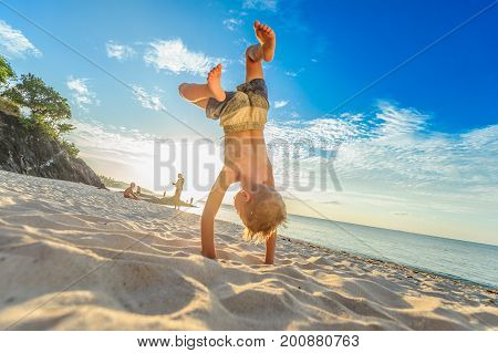 Handsome Eight Years Boy On Beach Performs Acrobatic Sketches And Plays With A Stream Of Sand