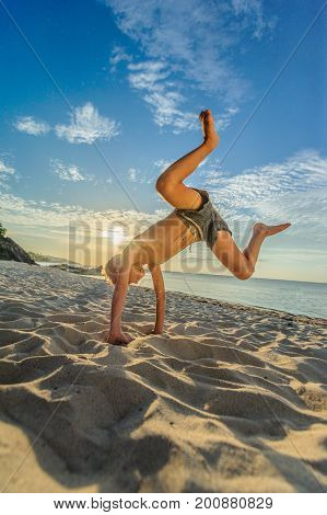 Handsome Eight Years Boy On Beach Performs Acrobatic Sketches And Plays With A Stream Of Sand