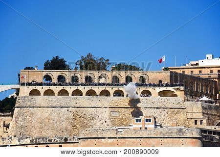 VALLETTA, MALTA - MARCH 31, 2017 - Firing of the Noon Gun in Upper Barrakka Gardens seen from across the Grand Harbour in Vittoriosa with tourists watching on Valletta Malta Europe, March 31, 2017.