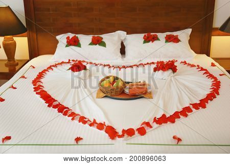 Bed with flowers and fruits in hotel room prepared for romantic date