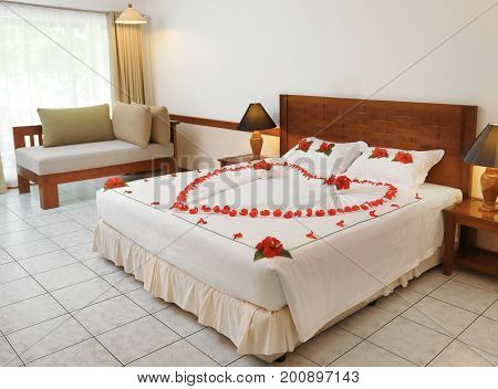 Bed decorated with heart made of flowers in hotel room