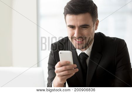 Attractive smiling businessman looking at smartphone in his hand, texting, sending messages on cellphone, using easy banking app, checking daily calendar or personal organizer, mobile office. Portrait
