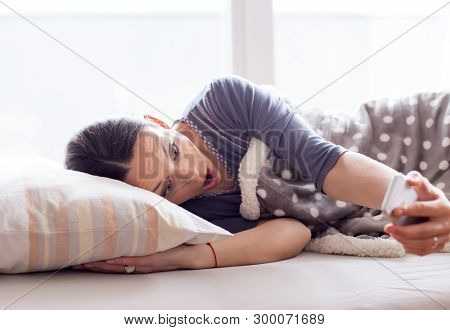 Girl In Bed Looking At Mobile Phone With Chocked And Panic Face Expression. Oversleep And Getting La