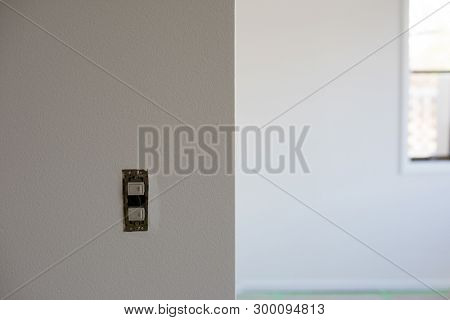 A room in process of renewing wallpaper. White room with new fresh wall paper and window in background. wall has switch with switch plates detached. 