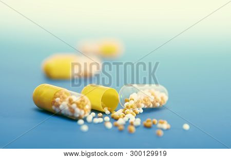 Split-open Yellow Capsule On Blue Gradient Background, Text Space. This Image Is Toned.