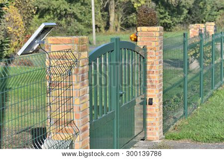 Fence With A Green Electric Gate Way In A Garden