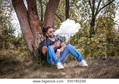 Stylish Brutal Vape Man Enjoying An E-cigarette In The Woods. Handsome Man.
